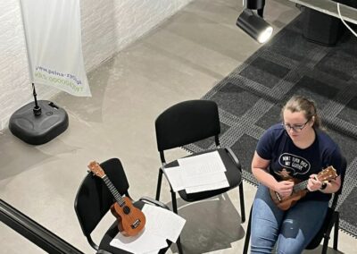 Prowadząca zajęć instruuje uczestników jak grać na ukulele