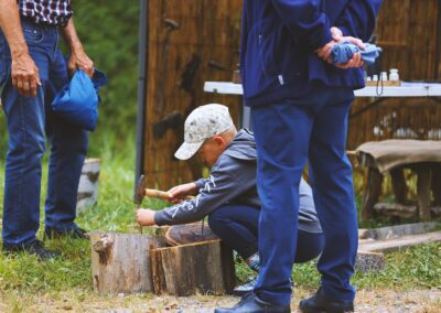 Chłopczyk wbija gwoździe w pieniek pod czujnym okiem dorosłego